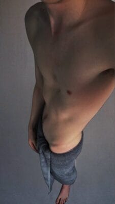 Shirtless young man standing torso-forward, wearing gray sweatpants, bare feet, viewed from above.